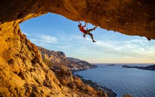 Male Climber On Overhanging Rock Against Beautiful View Of Coast Below  Wall Mural