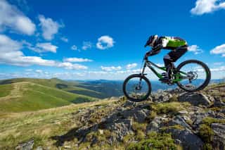 A Man Is Riding Bicycle, On The Background Of Mountains And Blue Sky  Beautiful Summer Day    Wall Mural