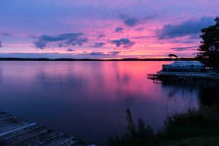 Colorful Pink, Purple & Blue Sunset Over A Calm Lake With A Pontoon Boat At The Shore  Beautiful Northwoods Scene With A Colorful Sky Reflected In The Water  Concepts Of Vacation, Nature, Travel Wall Mural