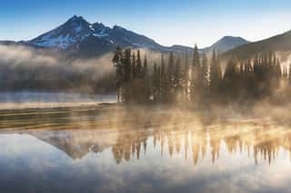 South Sister And Broken Top Reflect Over The Calm Waters Of Sparks Lake At Sunrise In The Cascades Range In Central Oregon, USA In An Early Morning Light  Morning Mist Rises From Lake Into Trees   Wall Mural