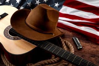 American Culture, Living On A Ranch And Country Muisc Concept Theme With A Cowboy Hat, USA Flag, Acoustic Guitar, Harmonica And A Rope Lasso On A Wooden Background In A Old Saloon Wall Mural