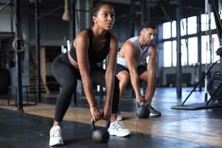 Fit And Muscular Couple Focused On Lifting A Dumbbell During An Exercise Class In A Gym    Wall Mural