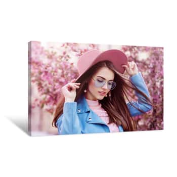 Image of Young Beautiful Fashionable Girl Wearing Stylish Blue Color Aviator Sunglasses, Pink Suede Hat, Earrings, Biker Jacket  Model Posing In Street With Flowering Trees  Spring Fashion Concept Canvas Print